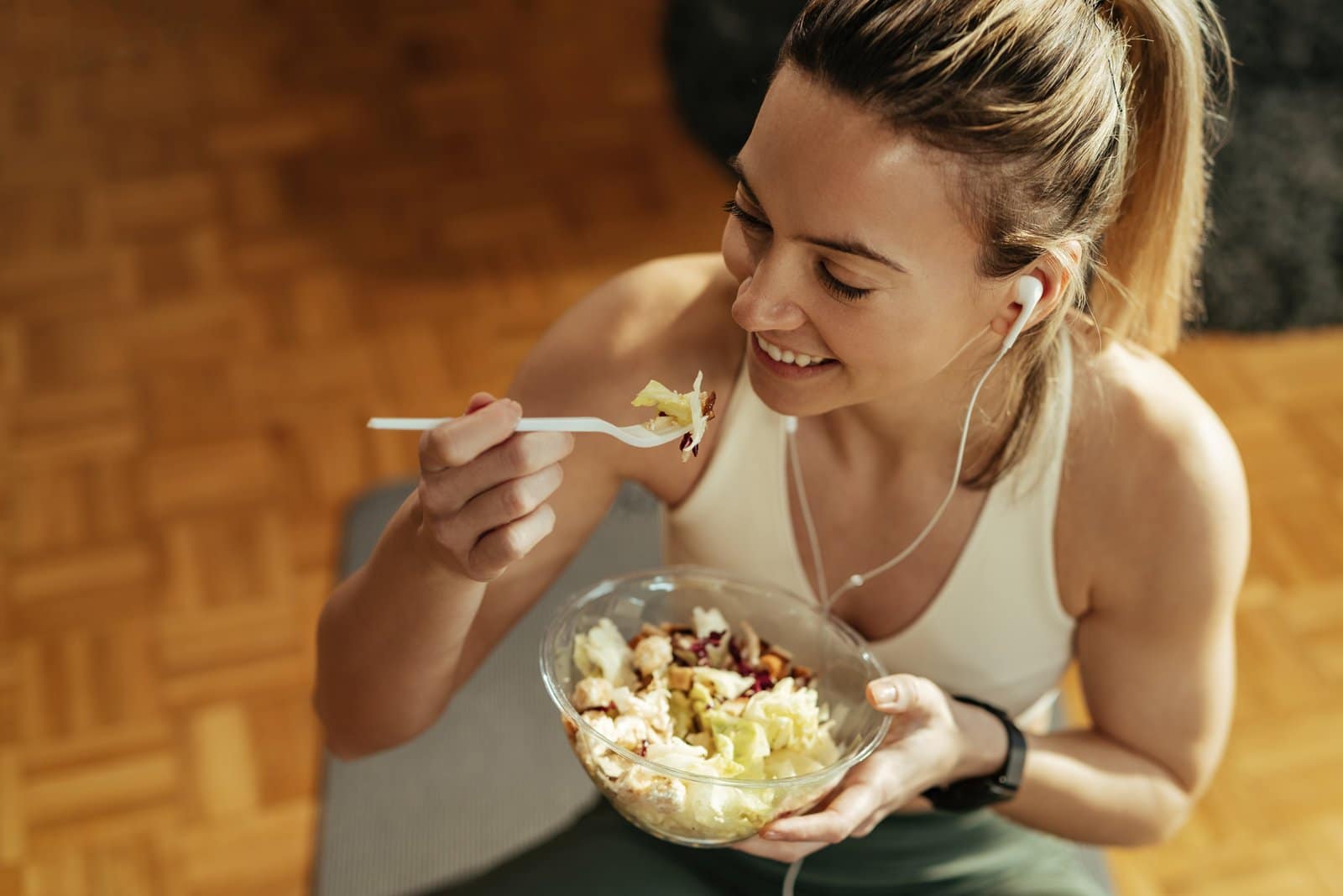 above view of happy sportswoman eating salad after the workout.